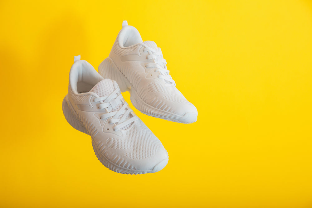 floating white mesh running shoes against yellow background