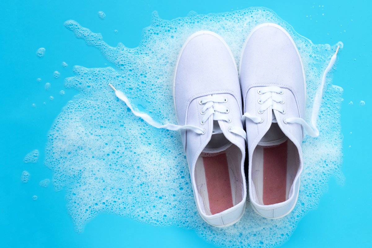 White canvas shoes cleaned with SneakERASERS Soak on a soapy blue background.